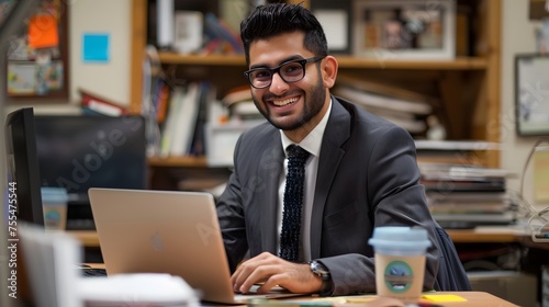 Smiling businessman wearing glasses in suit sitting using a laptop in a comfortable office. looking at camera, front side view.  photo