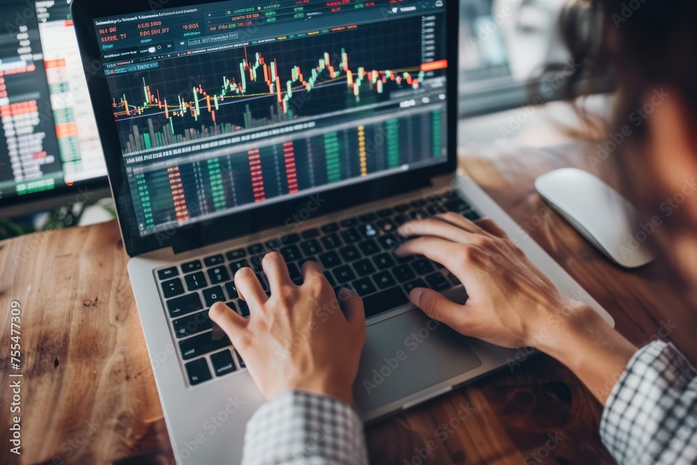A person is typing on a laptop computer with a stock market graph displayed on the screen. The person appears to be focused on the screen A person is typing on a laptop computer with a stock market graph displayed on the screen. The person appears to be focused on the screen