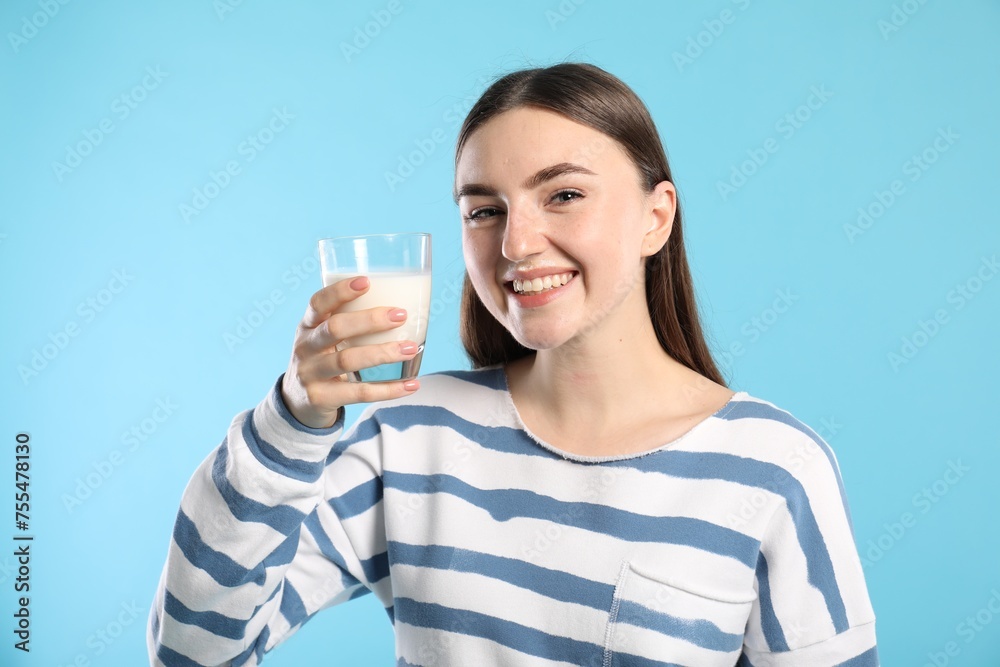 Happy woman with milk mustache holding glass of tasty dairy drink on light blue background Happy woman with milk mustache holding glass of tasty dairy drink on light blue background