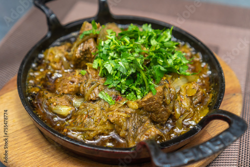 Close-up of the traditional Georgian dish ostri sprinkled with herbs in a cast-iron pan on a wooden board on the table. photo