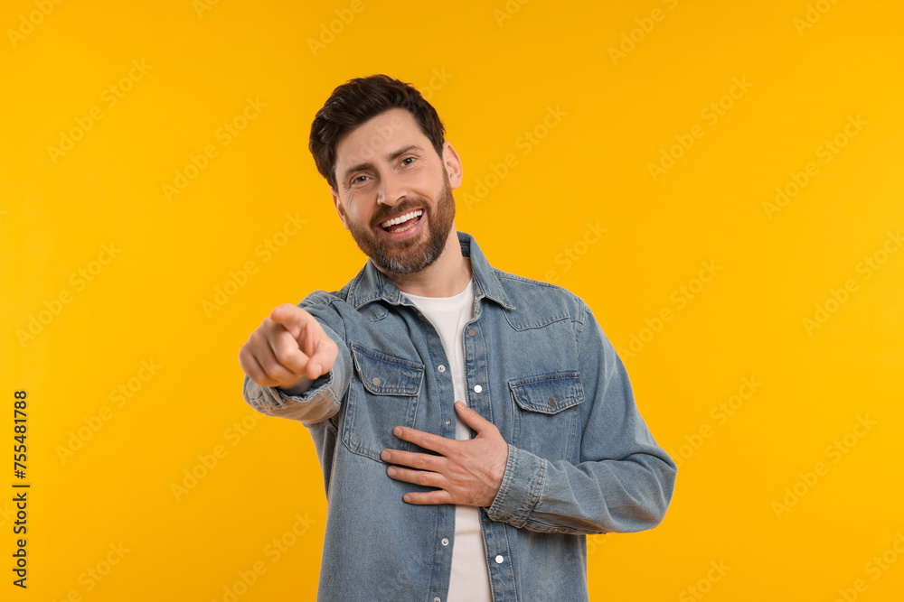 Handsome man pointing at something and laughing on yellow background Handsome man pointing at something and laughing on yellow background