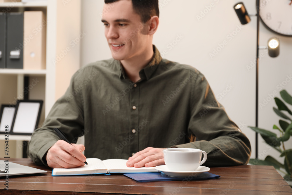 Man taking notes at wooden table in office, selective focus