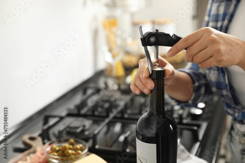 Woman opening wine bottle with corkscrew indoors, closeup. Space for text