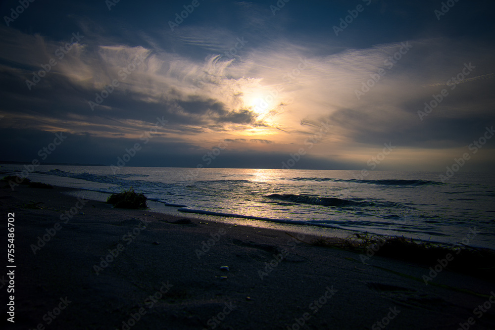 Sunset, illuminated sea. Sandy beach in the foreground. Light waves. Baltic Sea