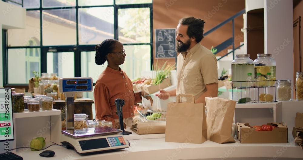 Vendor helping people with information about homegrown produce and sustainable lifestyle, presenting organic natural food choices. Couple looking for vegan alternatives at local eco store.