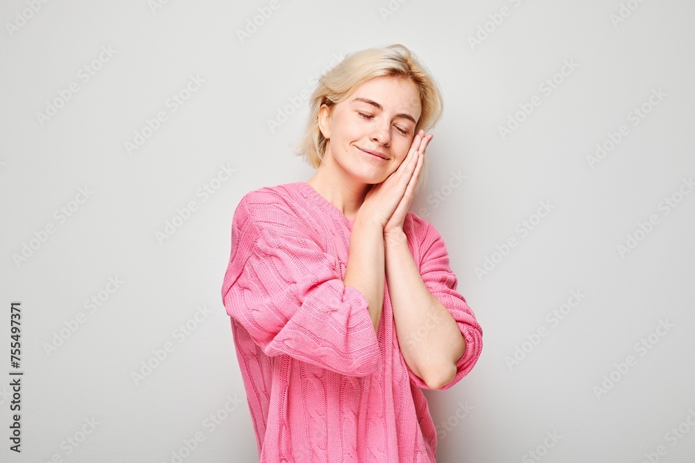 Woman with closed eyes smiling pretending to sleep with hands under cheek on gray background. Woman with closed eyes smiling pretending to sleep with hands under cheek on gray background.