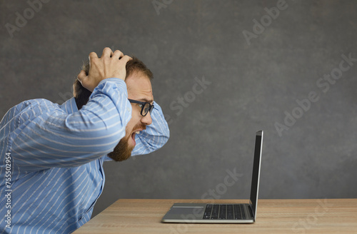 Konstfotografi Side profile view man sitting at desk, holding head in hands, looking at laptop screen in despair