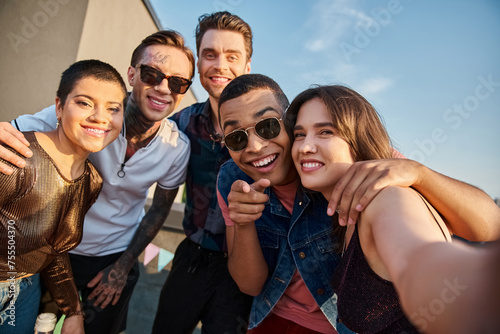 attractive jolly multiracial friends posing together on rooftop and smiling happily at camera