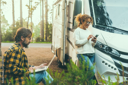 Adult couple of traveler enjoy outdoors leisure activity together outside a modern motorhome camper van parking in the forest. Freedom and remote work concept vanlife lifestyle. Parking destination photo