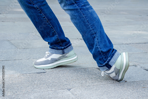 woman's feet in jeans and sneakers tripping over unevenly laid paving slabs. Accident injury on walk