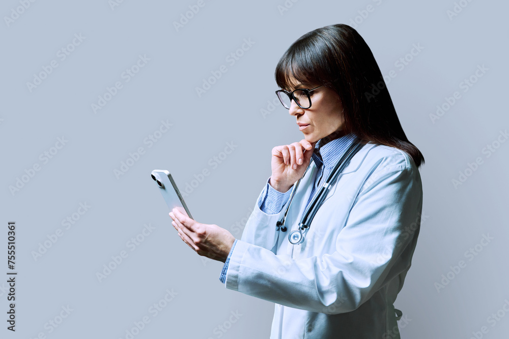 Profile portrait of female doctor using smartphone on gray background Profile portrait of female doctor using smartphone on gray background
