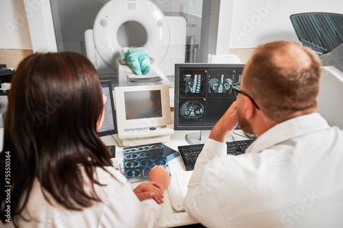 Medical computed tomography or MRI scanner. Back view of two doctors sitting  working at computer  making MRI. Two specialists consulting  talking  thinking  looking. Concept of modern diagnostics.