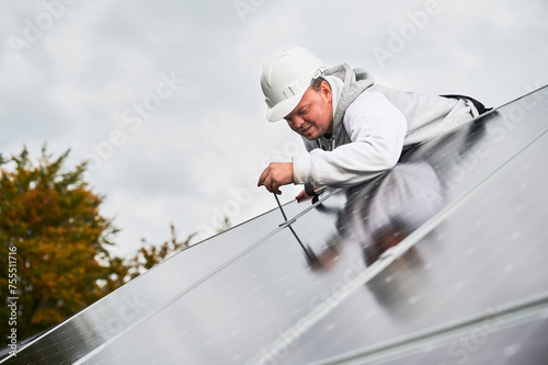 Man worker mounting photovoltaic solar panels on roof of house. Engineer in helmet installing solar module system with help of hex key. Concept of alternative, renewable energy.