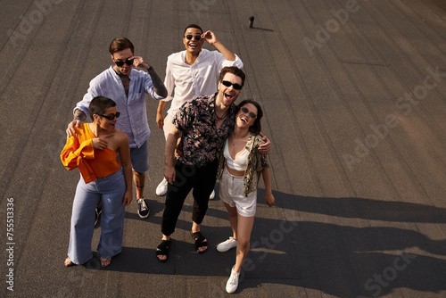 five interracial cheerful friends in vibrant attires posing on rooftop and smiling happily at camera © LIGHTFIELD STUDIOS