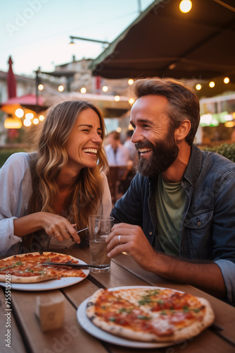 Happy young adult couple have fun eating a pizza together outdoor in traditional italian pizzeria restaurant sitting and talking and laughing. People enjoying food and dating relationship. Tourists