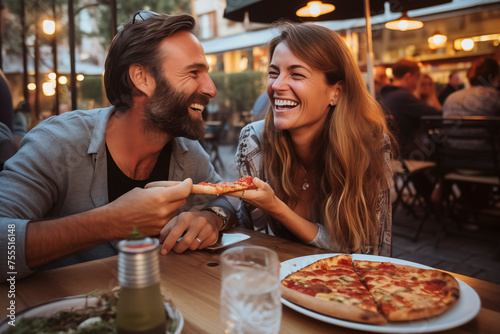 Happy young adult couple have fun eating a pizza together outdoor in traditional italian pizzeria restaurant sitting and talking and laughing. People enjoying food and dating relationship. Tourists photo