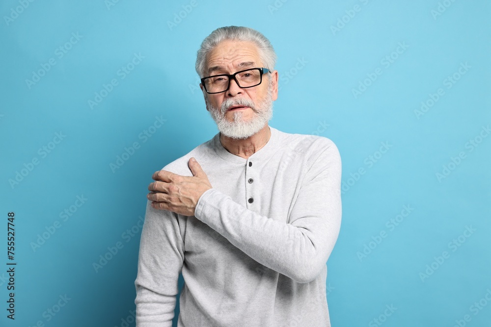 Arthritis symptoms. Man suffering from pain in shoulder on light blue background Arthritis symptoms. Man suffering from pain in shoulder on light blue background