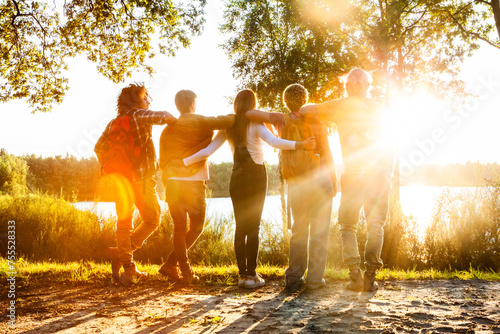 Backlit by the golden sun, a group of five friends shares an embrace, overlooking a peaceful lake. Friends Embracing the Sunset by a Serene Lakeside. High quality photo photo