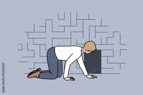 Man searching exit from labyrinth, crawling on floor near miniature door, as metaphor for difficult life situation. Guy is looking for way out of labyrinth, and needs hint or help.