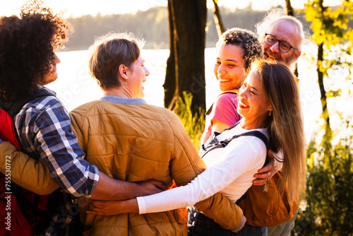 This image exudes warmth and camaraderie as a group of multiethnic friends share a group hug by the lakeside during sunset. Their smiling faces and the closeness of their embrace reflect strong bonds photo