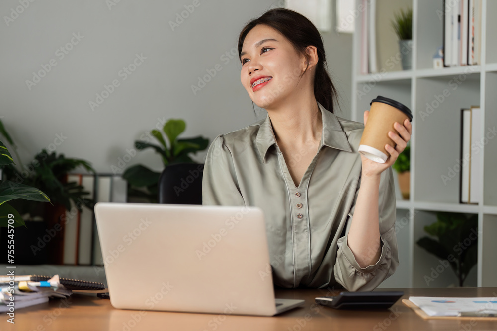 smiling businesswoman drinking coffee and working on laptop in green modern office. Nice Environment Office. Eco-Friendly Concept smiling businesswoman drinking coffee and working on laptop in green modern office. Nice Environment Office. Eco-Friendly Concept