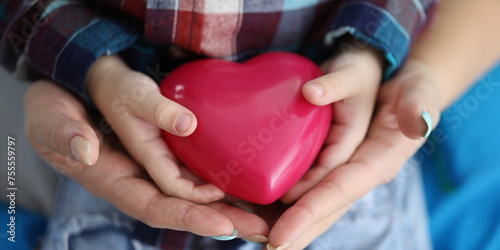 Woman and child hands holding red toy heart closeup. Save child life concept