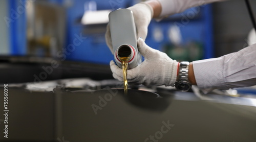 Master repairman pouring engine oil under hood of car closeup. Motor oil change interval concept