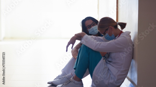 Tired women doctors wearing protective medical masks sitting in clinic corridor. Stress at work of medical staff concept
