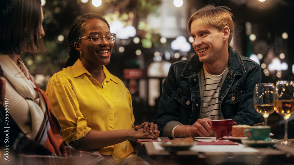 Fototapeta premium Young African Female Telling Empowering Personal Experience Stories While Sitting on Terrace. Young Men and Women Gathered in a Cafe in the Evening, Clapping and Celebrating the Success of a Friend