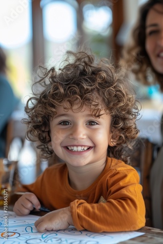 A toddler with a charming curly hair smiling and looking at camera  surrounded by his parents  with drawings on the table in a cozy home environment.