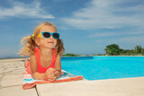 Young girl enjoys pool day with sunglasses, lay down on edge