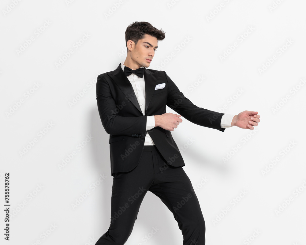 cool elegant businessman in black tuxedo holding hands to side