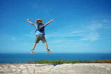 Happy blond kid with backpack jump high excited to see ocean