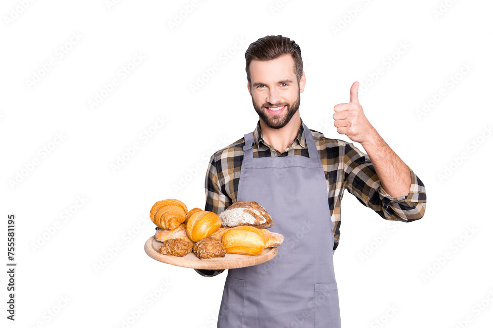 Portrait of positive attractive baker in uniform with stubble holding tray with bakery products in hand, showing thumb up with finger, isolated on grey background Portrait of positive attractive baker in uniform with stubble holding tray with bakery products in hand, showing thumb up with finger, isolated on grey background