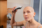 Hairless lady look at camera uses electric razor to shave head