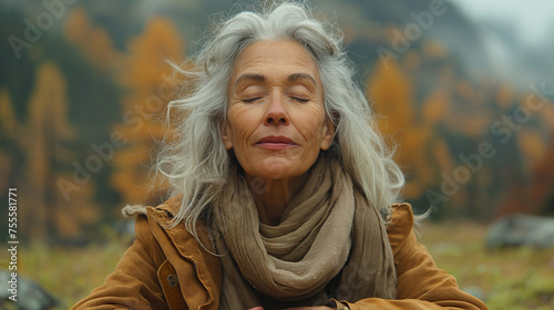 Head shot portrait close up of middle age woman enjoying and relaxing sitting at table in the nature in the forest of mountain. Old female person opening arms and closing eyes feeling free