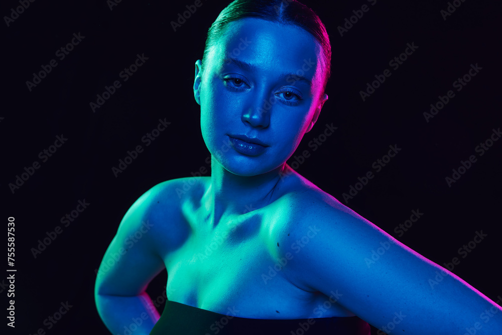 Portrait of young attractive woman with bare shoulders looking at camera in neon light against black studio background. UV protection. Concept of wellness, spa procedures, cosmetology, antiaging. Ad Portrait of young attractive woman with bare shoulders looking at camera in neon light against black studio background. UV protection. Concept of wellness, spa procedures, cosmetology, antiaging. Ad