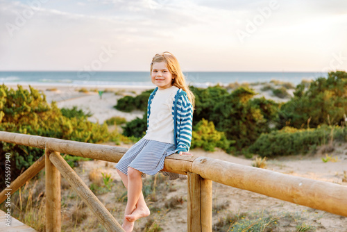 Adorable happy smiling little girl on beach vacation at sunset. Handsome cute preschool child with long blond hairs having fun on family vacations. © Irina Schmidt