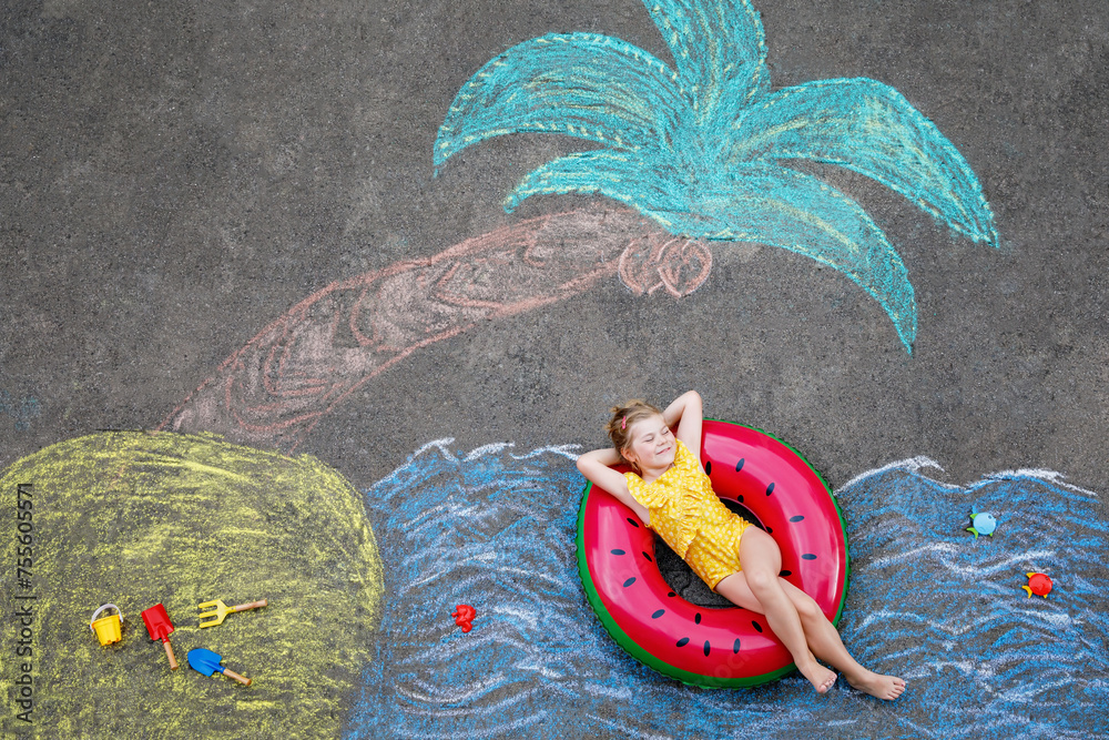 Φωτογραφία Happy little preschool girl in swimsuit on inflatable ring with sea, sand, palm painted with colorful chalks on asphalt