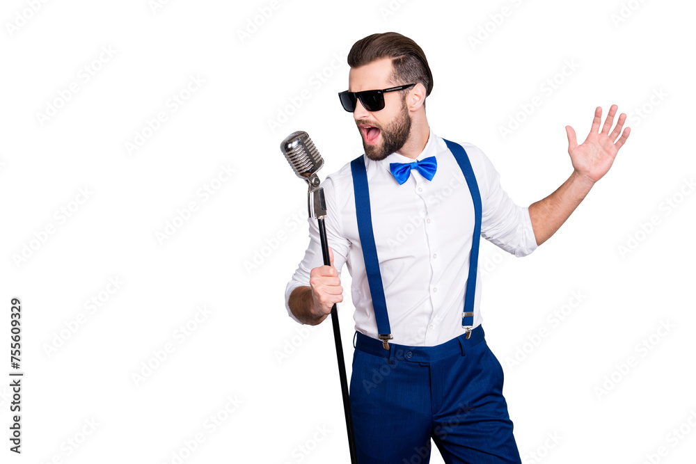 Portrait of handsome attractive singer in blue pants with suspenders and black glasses, singing hit with open mouth in microphone gesture with hand isolated on grey background Portrait of handsome attractive singer in blue pants with suspenders and black glasses, singing hit with open mouth in microphone gesture with hand isolated on grey background