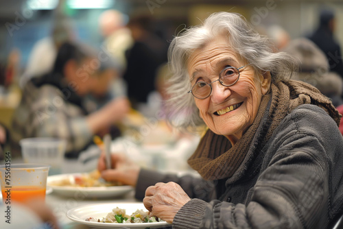 Cheerful elderly homeless woman eats free meal in spacious dining hall. Old lady in need visits soup house to get food. Volunteer care of houseless photo