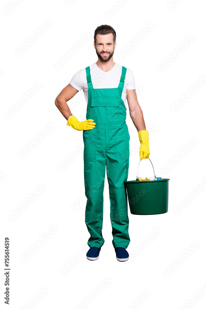 Full size fullbody portrait of joyful cheerful housekeeper with stubble, hairstyle in green uniform, isolated on grey background, having bucket with detergents, holding arm on waist Full size fullbody portrait of joyful cheerful housekeeper with stubble, hairstyle in green uniform, isolated on grey background, having bucket with detergents, holding arm on waist