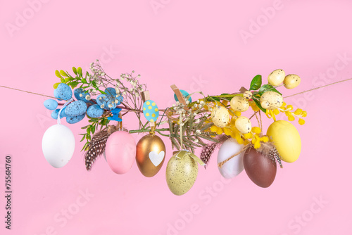 Creative bright spring Easter holiday concept. Painted Easter eggs, spring flowers, leaves and decorations hang on clothesline, bright sunny light copy space on pick colored background