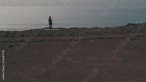 Girl doing yoga at the edge of the cliff by the ocean, sunset, aerial moving in shot, Fuerteventura Spain