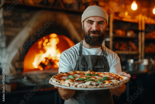 pizza maker holds ready-made beautiful pizza with basil c against the background of a wood-burning oven