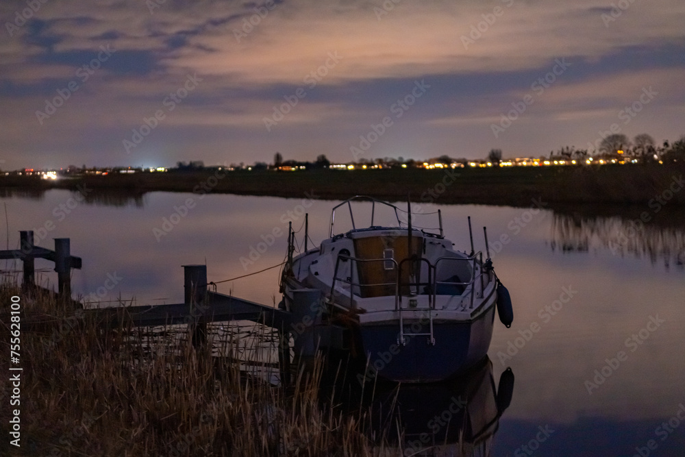 A boat anchored among the reeds at the edge of the river. Night landscape in a rural environment with a starry sky somewhere in the Netherlands