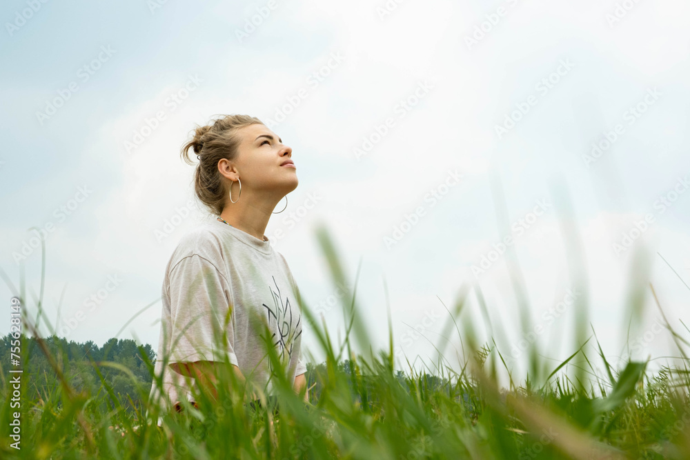 Young woman sitting in the grass and looking at the sky. Lifestyle concept Young woman sitting in the grass and looking at the sky. Lifestyle concept