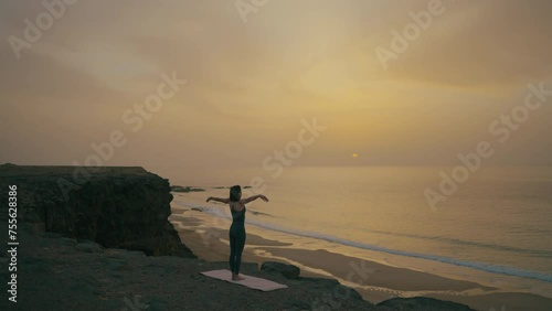 Woman doing yoga on the edge of the cliff by the ocean at sunset, Fuerteventura, Spain