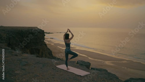 Woman doing yoga on the edge of the cliff by the ocean at sunset, Fuerteventura, Spain