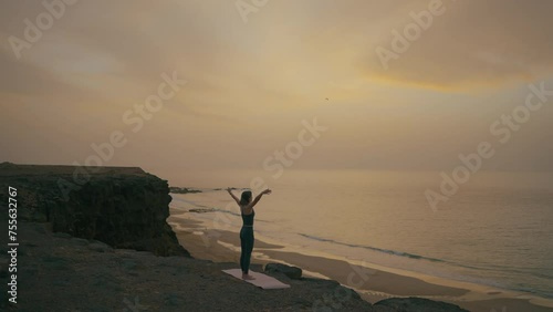 Woman doing yoga on the edge of the cliff by the ocean at sunset, Fuerteventura, Spain